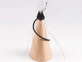 Cardboard cone with beaded wire spiraling around the top showing insertion of the next vertical wires